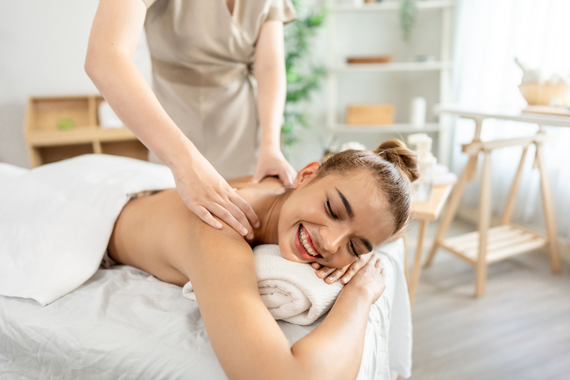 Beautiful woman getting back massage treatment with oil at beauty spa. Attractive young girl lying down on massage bed getting relaxing physiotherapy service from masseuse for body in spa clinic.