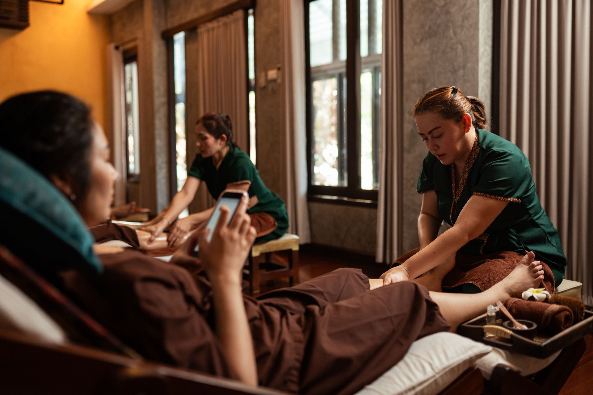 Professional Masseuse mature asian woman working service foot massage to customer in spa salon, Massage customer chatting with smartphone, Relaxing massage in cosmetology spa centre.