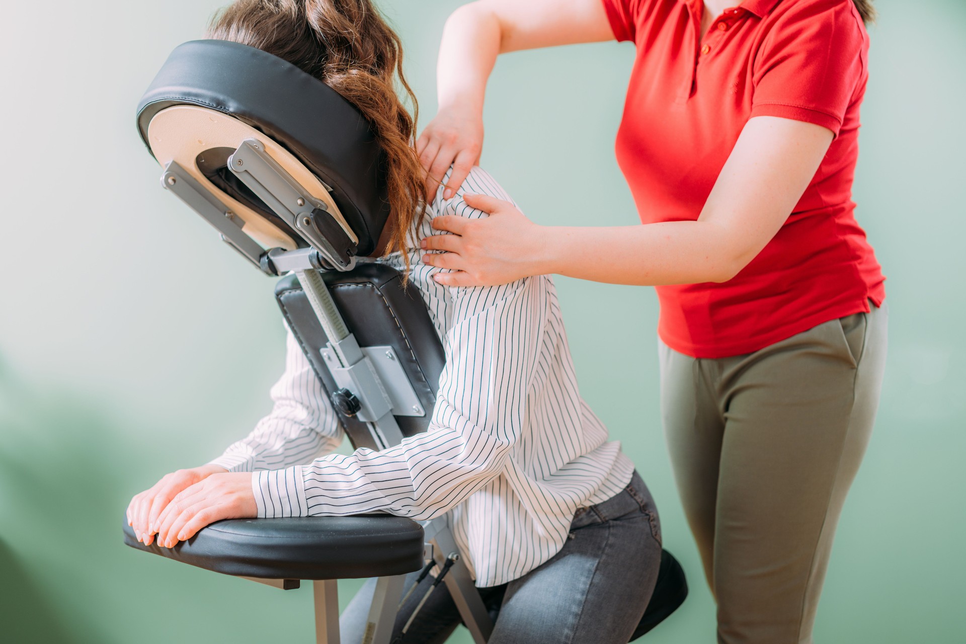 Female employee sitting on a portable massage chair in business office. Therapist massaging her shoulders, releasing muscle tension.